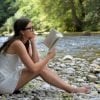 This shows a woman reading a book by a river