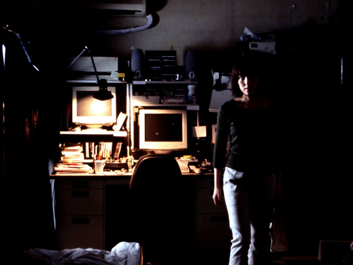 A young woman stands in front of a computer, in shadows.