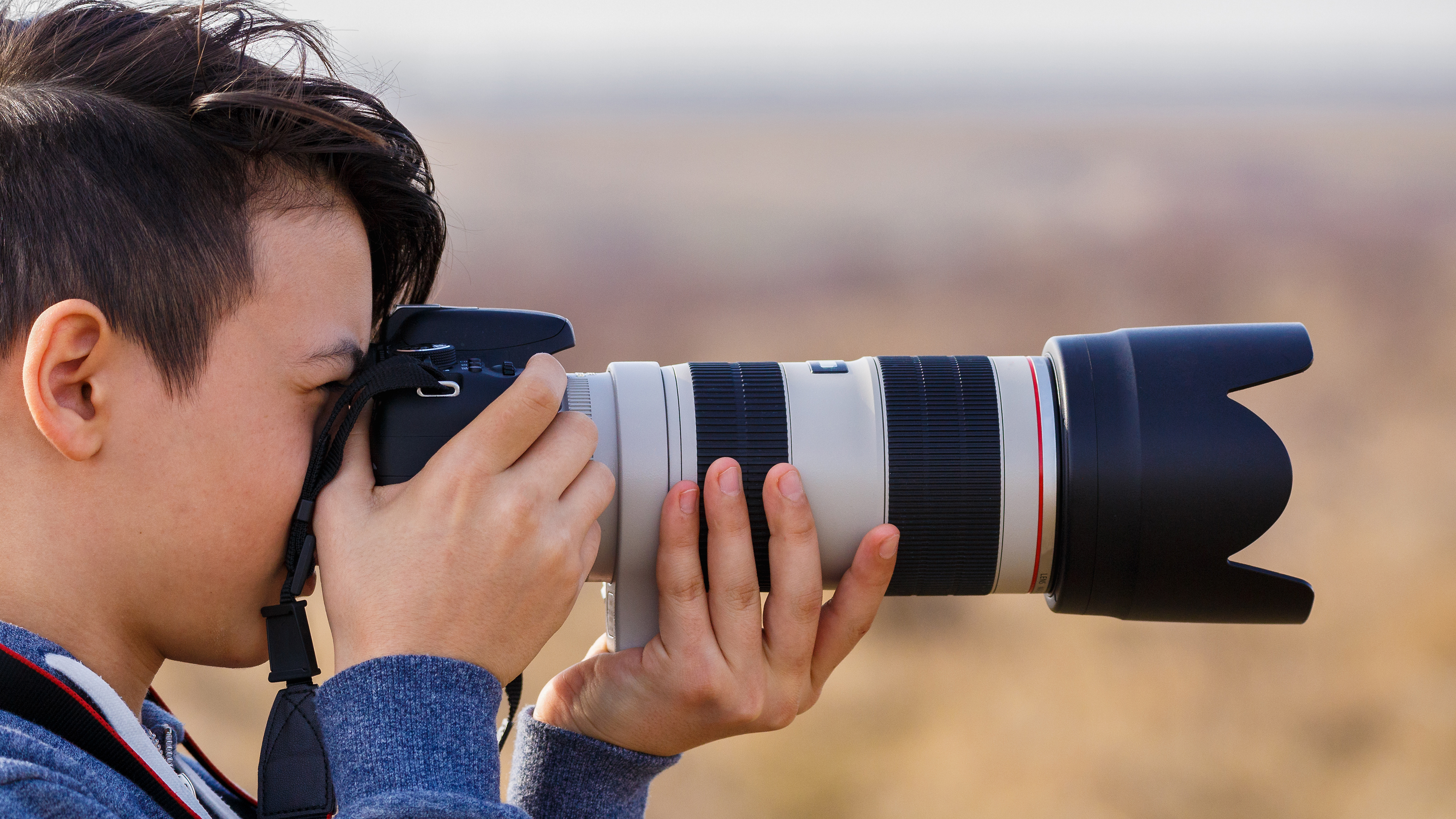 A man holding a DSLR with a telephoto lens to his eye